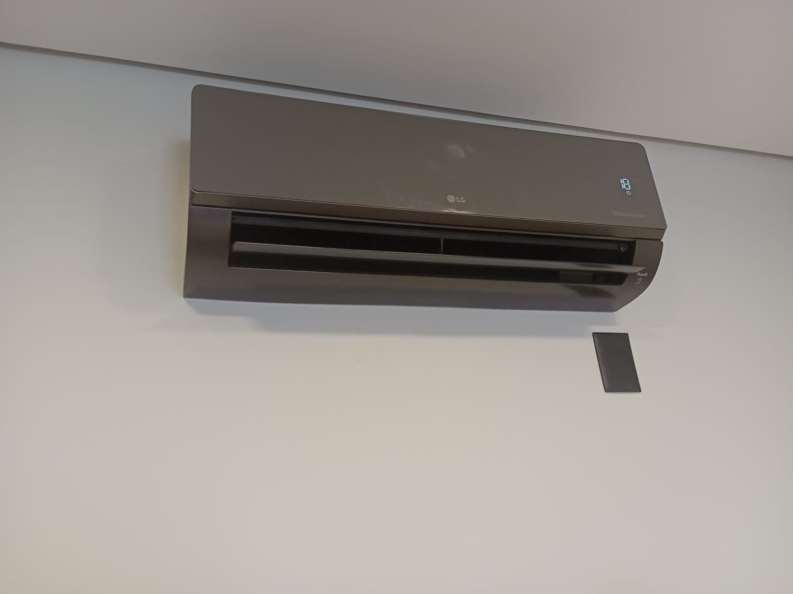Split LG na cor grafite instalado, com o controle remoto ao lado